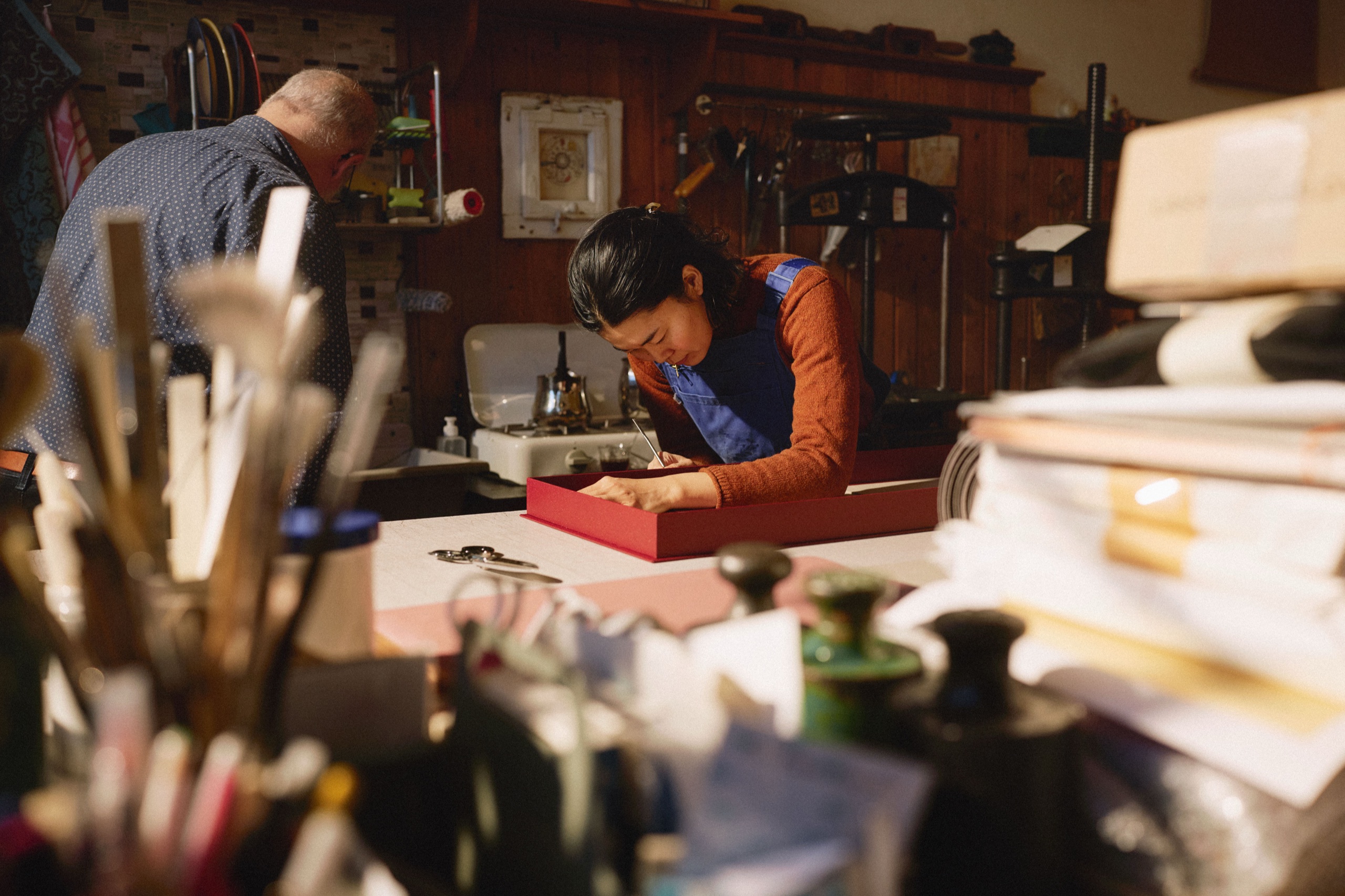 A bookbinder closes a hand-bound red slipcase on a workshop table