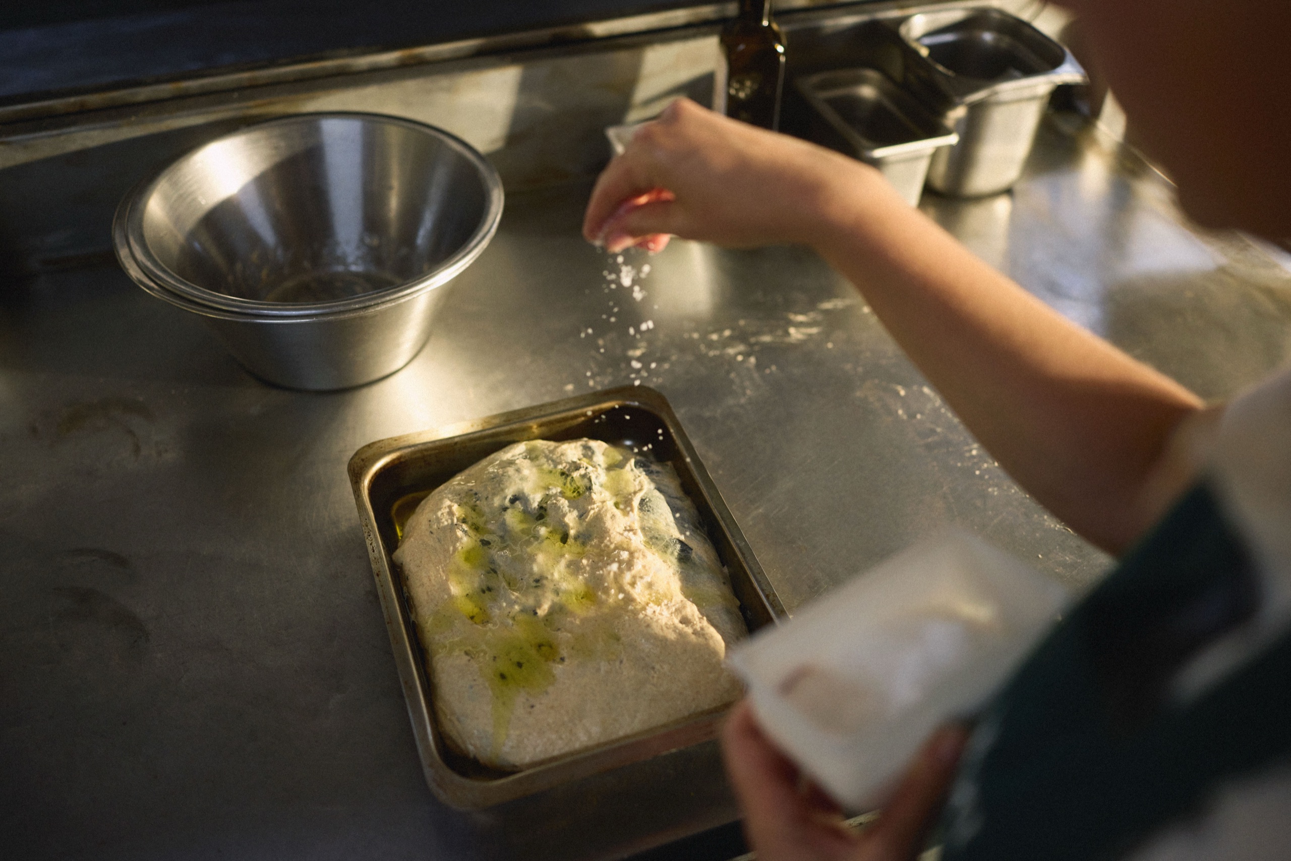 A hand salts focaccia dough in warm kitchen light