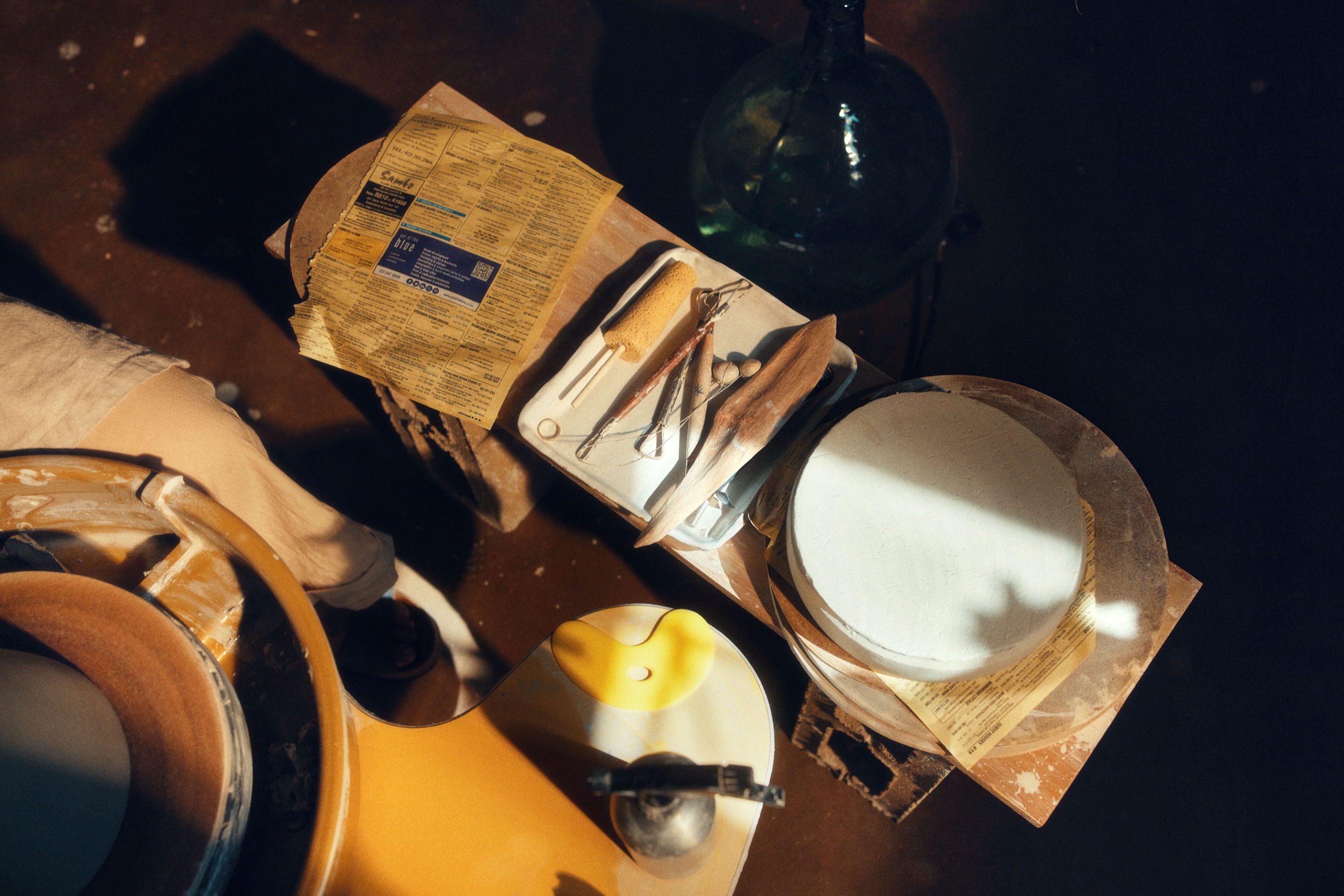 Top-down view of pottery tools and a covered form on a workbench