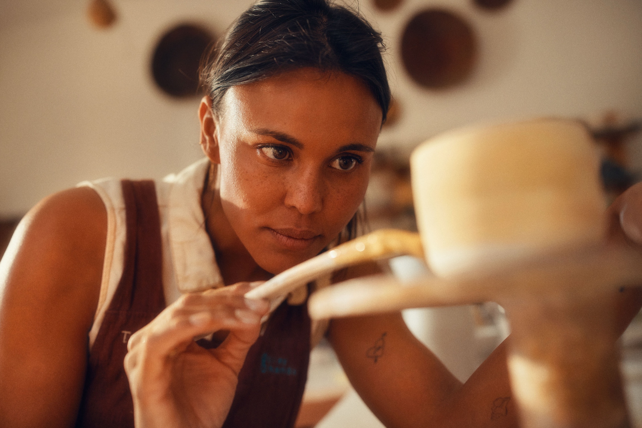 A ceramicist trims a pot at the wheel, focused in warm side light